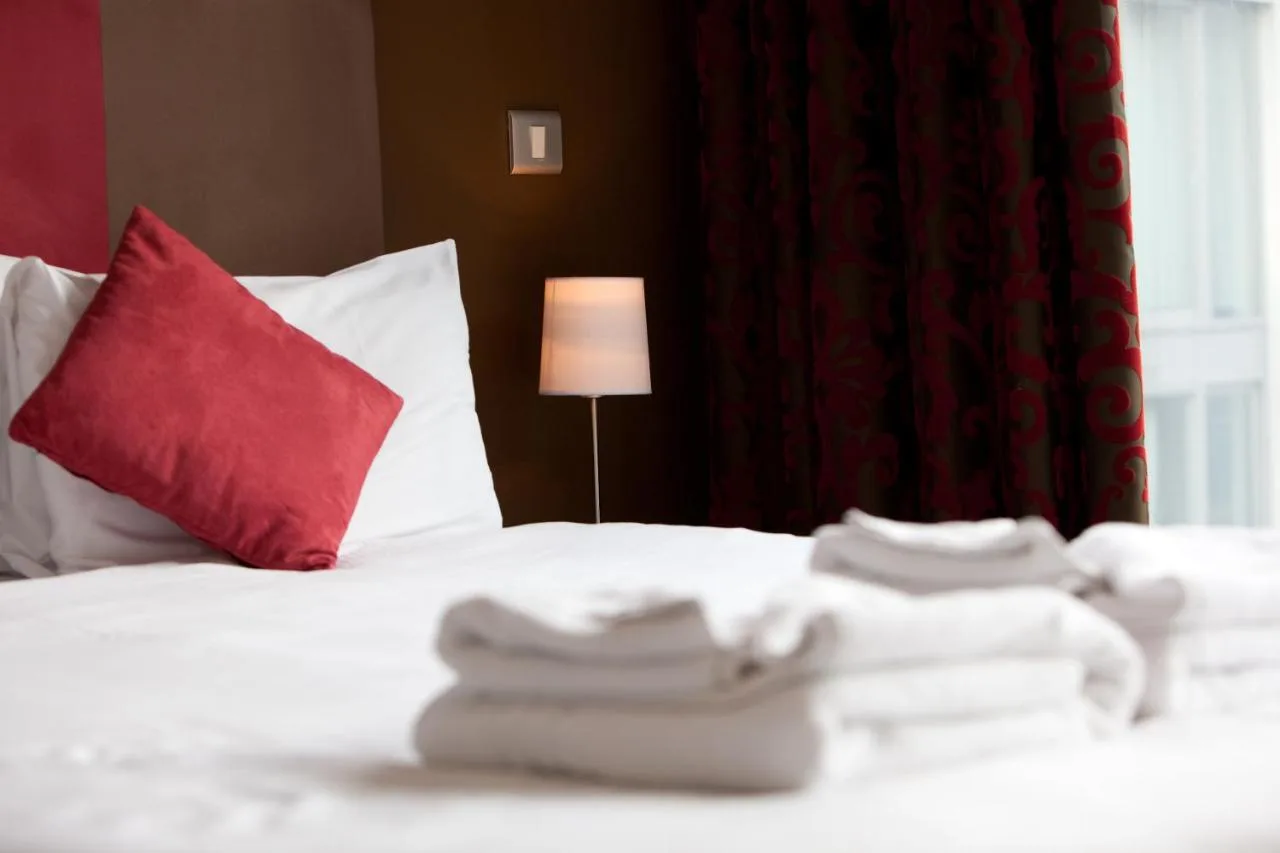a white bed with a red pillow and a lamp at The Spires Serviced Apartments Birmingham in Birmingham