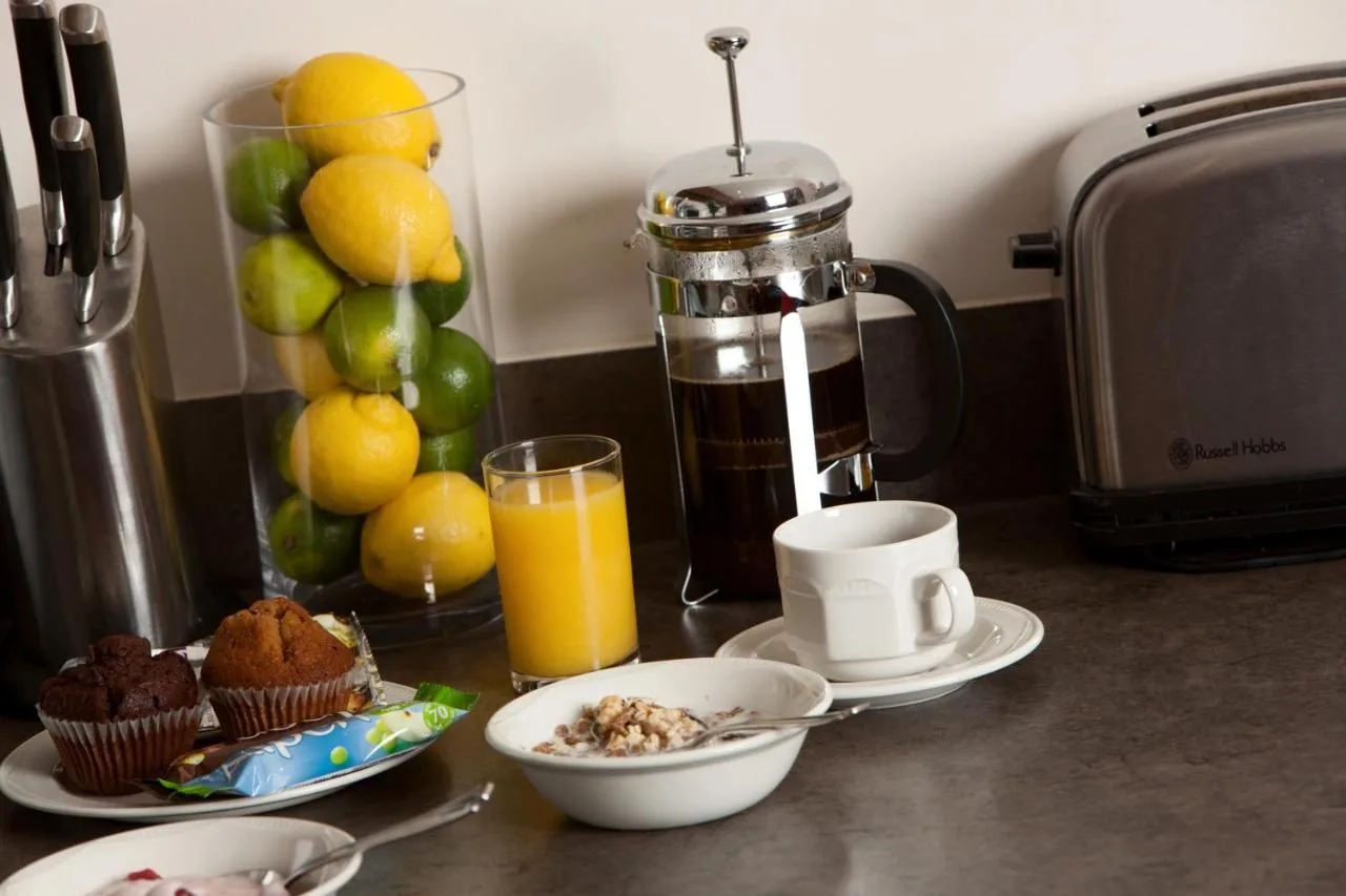 a kitchen counter with a breakfast of muffins and orange juice at The Spires Serviced Apartments Birmingham in Birmingham